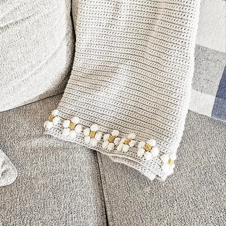 May include: A crocheted throw blanket with a white background and a border of small white and yellow crocheted flowers.