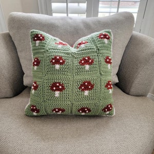 Puede incluir: Una almohada de crochet verde con un borde blanco y dise&ntilde;os de setas rojas.