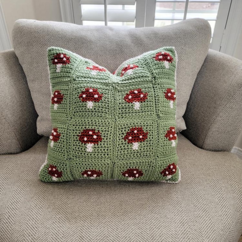 Puede incluir: Una almohada de crochet verde con un borde blanco y dise&ntilde;os de setas rojas.