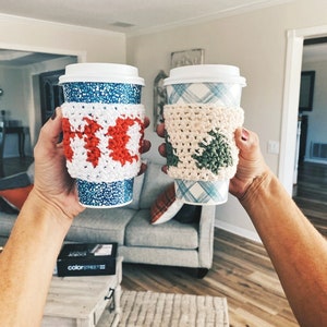 May include: Two coffee cups with crocheted cup cozies. One cozy is red and white and the other is green and white.