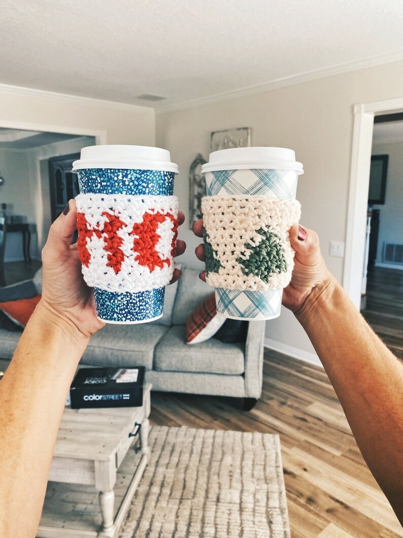May include: Two coffee cups with crocheted cup cozies. One cozy is red and white and the other is green and white.