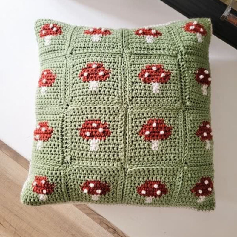 Puede incluir: Una almohada de punto de ganchillo verde con un patr&oacute;n de setas rojas y blancas.