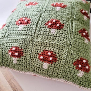 Puede incluir: Una almohada de punto de ganchillo verde con un borde blanco y dise&ntilde;os de setas rojas y blancas.