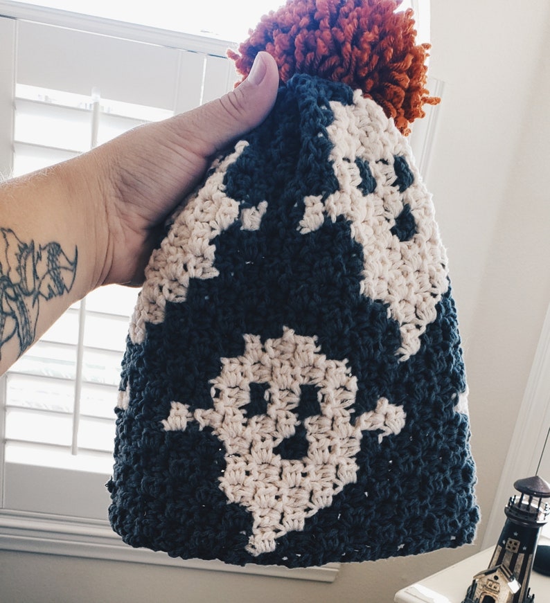 May include: A crocheted hat with a dark blue and white pattern and a large orange pom-pom on top.