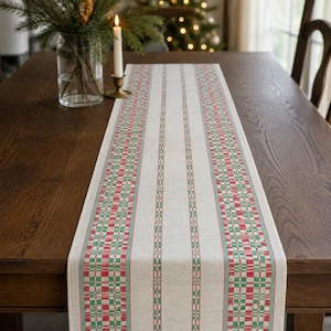 Puede incluir: Un camino de mesa rectangular con una base tejida en color blanco roto y rayas verticales. El patrón incluye bandas alternas de cuadros rojos y verdes separadas por finas líneas verdes sólidas, creando un diseño estructurado y simétrico.