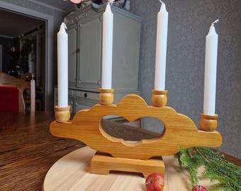 Puede incluir: Un candelabro de madera clara con cuatro velas blancas. El candelabro tiene un recorte en forma de corazón. Las velas son largas y delgadas. El candelabro se apoya en una base de madera.