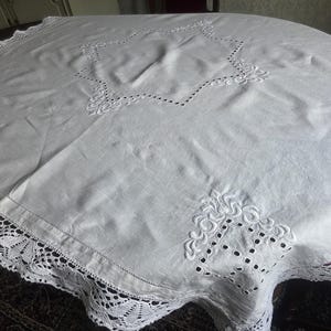 Könnte beinhalten: Weißer runder Tischläufer mit gestickten Stern- und Blumenmustern. Der Tischläufer hat eine zarte Spitzenborte am Rand, die einen Hauch von Eleganz verleiht. Der Stoff scheint ein weiches, gewebtes Material zu sein.