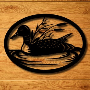 May include: Black metal wall art depicting a loon swimming in a lake with reeds and cattails. The loon is in silhouette and the background is a simple oval shape.