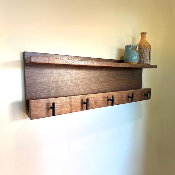 Solid walnut floating shelf with integrated coat hooks — the kind of entryway piece that looks like it belongs in a design magazine, not a big-box store.