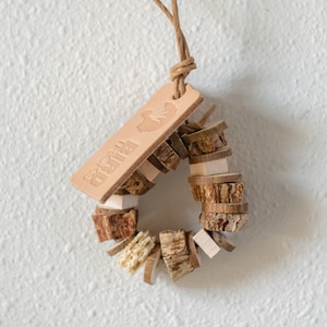 May include: A natural wood chew toy for small animals, shaped like a ring. The toy is made of different types of wood, including bark and branches. The toy is attached to a leather tag with the word "Birds" and a small bird silhouette.