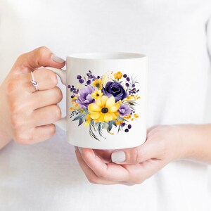 Op de afbeelding: Witte keramische mok met een bloemenontwerp met gele en paarse bloemen. De bloemen zijn geschilderd in aquarelstijl.