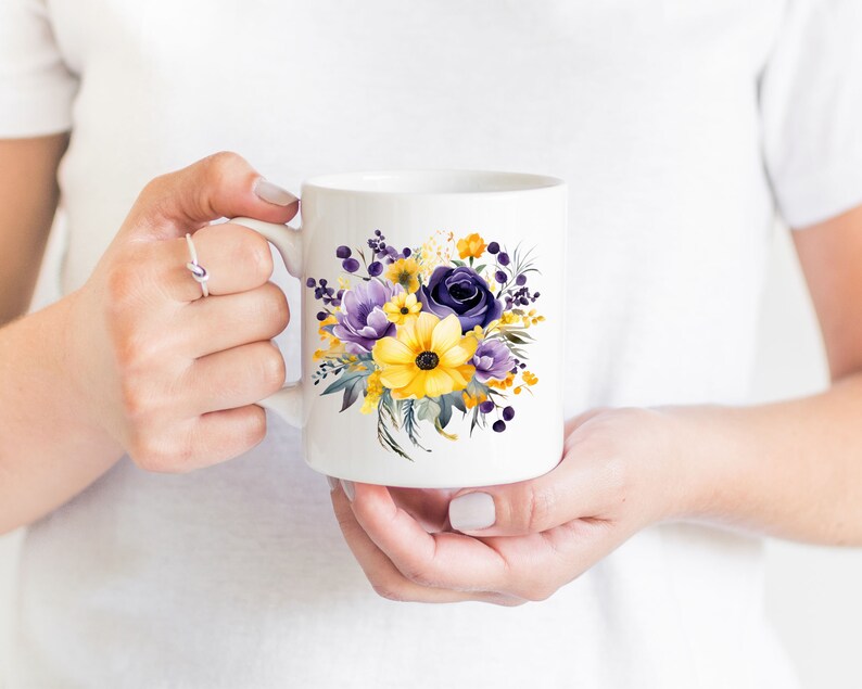 Op de afbeelding: Witte keramische mok met een bloemenontwerp met gele en paarse bloemen. De bloemen zijn geschilderd in aquarelstijl.