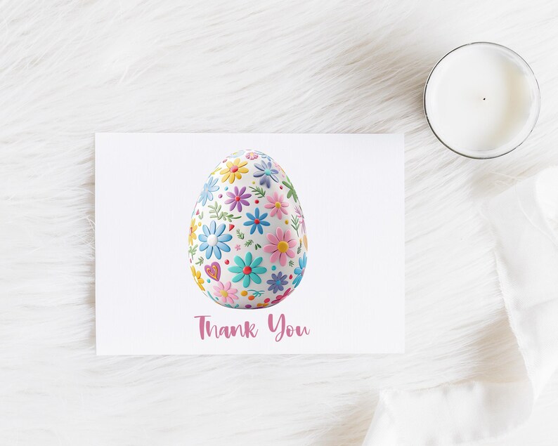 May include: A white greeting card with a floral Easter egg design and the words "Thank You" in pink script. The egg is covered in colorful flowers. A lit candle sits to the right.