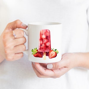 May include: White ceramic mug with a red and white strawberry popsicle design. The popsicle is filled with red fruit and has a wooden stick. There are two strawberries on either side of the popsicle.