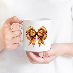 Pode incluir: Uma caneca de cer&acirc;mica branca com um grande desenho de la&ccedil;o laranja e preto. O la&ccedil;o tem um centro preto e &eacute; decorado com um padr&atilde;o floral.