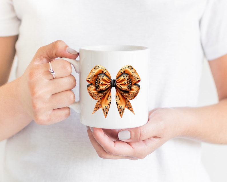 Pode incluir: Uma caneca de cer&acirc;mica branca com um grande desenho de la&ccedil;o laranja e preto. O la&ccedil;o tem um centro preto e &eacute; decorado com um padr&atilde;o floral.