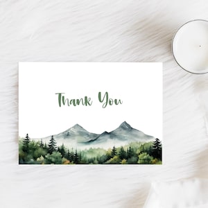 May include: A white card with the text "Thank You" printed in green. The card features a watercolor illustration of a mountain range with green trees in the foreground.