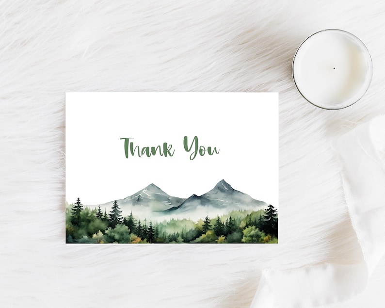 May include: A white card with the text "Thank You" printed in green. The card features a watercolor illustration of a mountain range with green trees in the foreground.