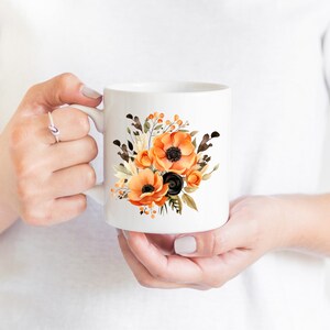 May include: White ceramic mug with a floral design featuring orange and black flowers. The flowers are watercolor style and have a vintage feel.
