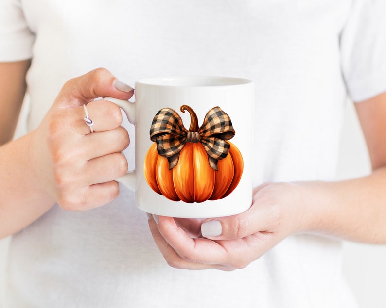 May include: White ceramic mug with a hand-painted orange pumpkin with a brown and black plaid bow.