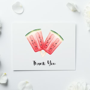 May include: A white card with a watercolor illustration of two watermelon popsicles. The popsicles are red with black seeds and green rinds. The words "Thank You" are written in black script below the popsicles. White flowers and petals surround the card.