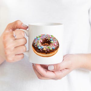 May include: White ceramic mug with a chocolate glazed donut with colorful sprinkles. The donut is on a white background.