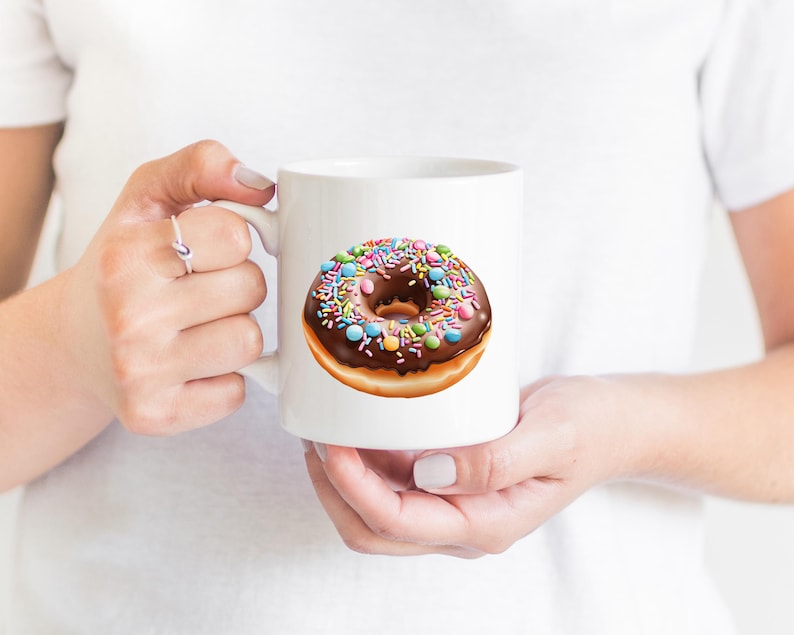 May include: White ceramic mug with a chocolate glazed donut with colorful sprinkles. The donut is on a white background.