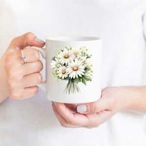 May include: White ceramic mug featuring a printed design of a bouquet of white daisies with yellow centres and green leaves.