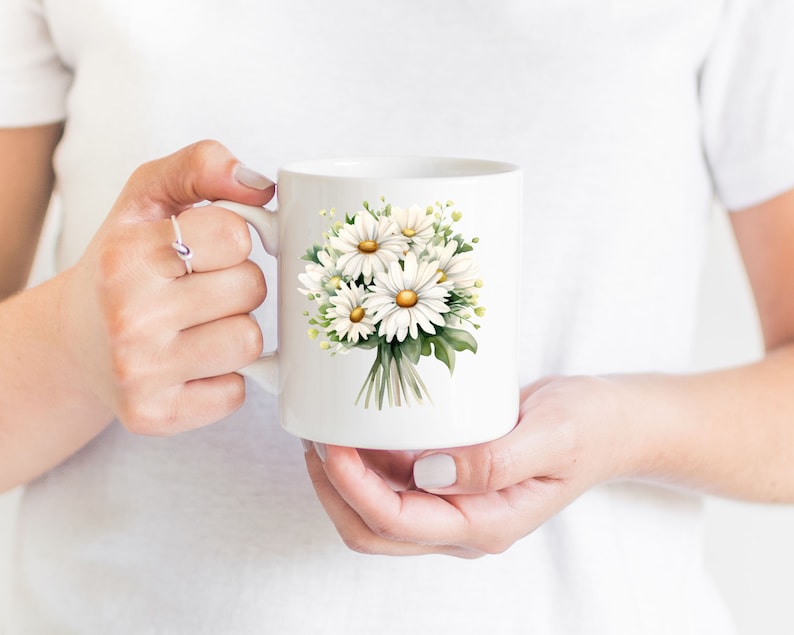 May include: White ceramic mug featuring a printed design of a bouquet of white daisies with yellow centres and green leaves.