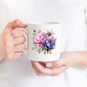 May include: White ceramic mug with a floral design featuring pink and purple flowers. The flowers are watercolor style and have green leaves.