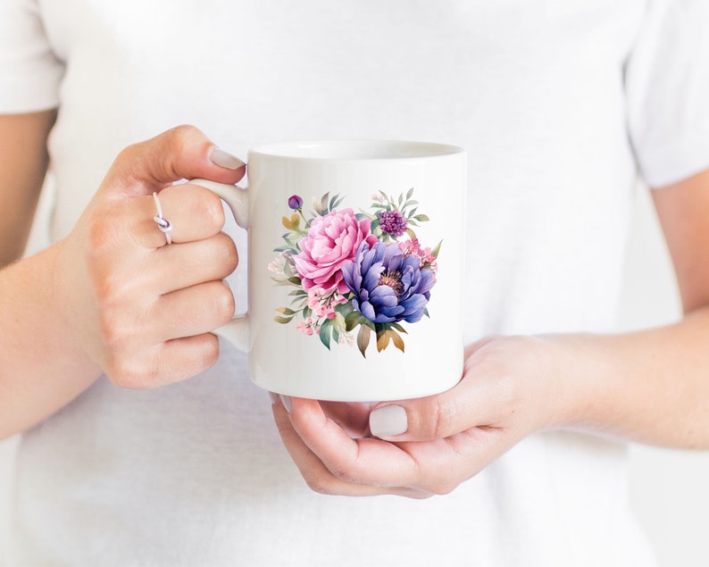 May include: White ceramic mug with a floral design featuring pink and purple flowers. The flowers are watercolor style and have green leaves.