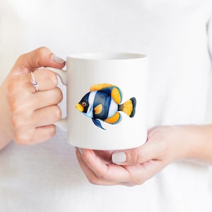 May include: White ceramic mug with a colorful illustration of a blue, yellow, and white fish. The fish has black stripes and yellow fins.