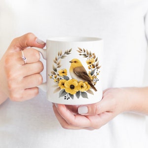 May include: White ceramic mug with a yellow bird and yellow flowers in a wreath design.