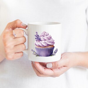 May include: White ceramic mug with a lavender cupcake design. The cupcake has purple frosting and is decorated with lavender flowers.