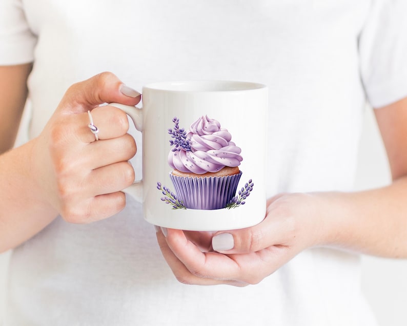 May include: White ceramic mug with a lavender cupcake design. The cupcake has purple frosting and is decorated with lavender flowers.