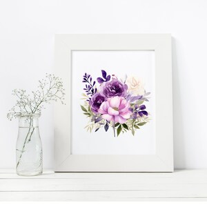 May include: A framed floral print showing a watercolour bouquet of purple and pink flowers, including roses and other blooms with green foliage. The print is in a white frame. A small glass vase with white flowers is to the left.