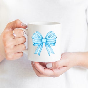 May include: White ceramic mug with a blue watercolor bow design.