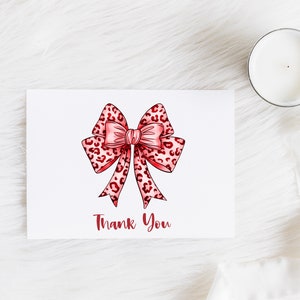 Puede incluir: Una tarjeta blanca con un lazo de estampado de leopardo rosa y rojo y el texto "Gracias" en rojo.