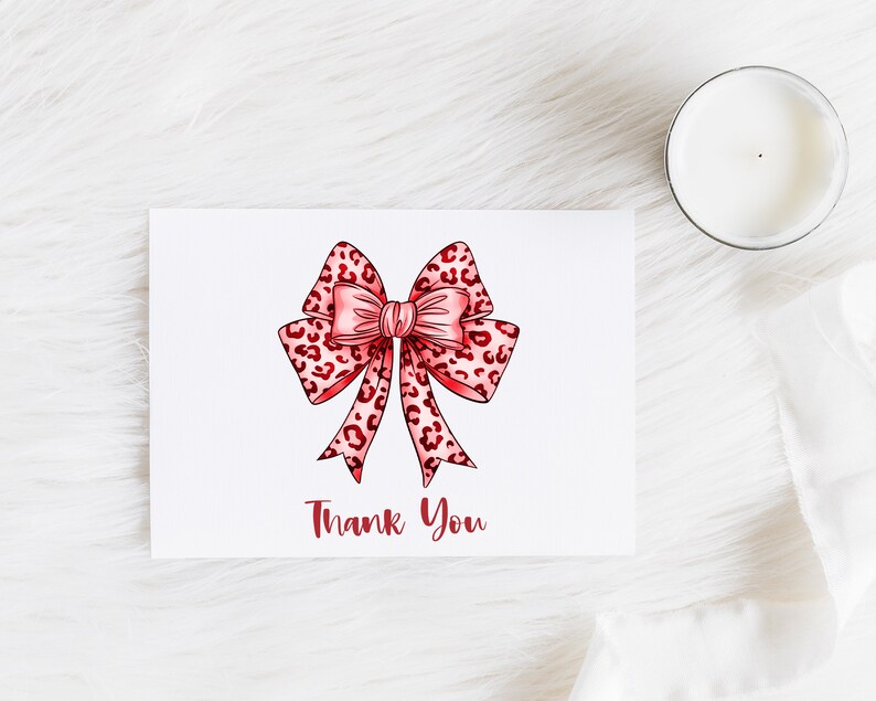 Puede incluir: Una tarjeta blanca con un lazo de estampado de leopardo rosa y rojo y el texto "Gracias" en rojo.