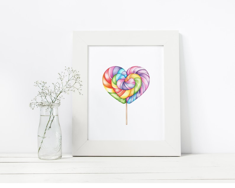 May include: A white framed print of a colorful heart-shaped lollipop on a stick. The lollipop is made of swirls of pink, purple, blue, green, and yellow.