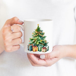 May include: White ceramic mug with a watercolor illustration of a green Christmas tree with gold ornaments and a red bow. The tree is surrounded by wrapped presents with red, green, and gold accents.