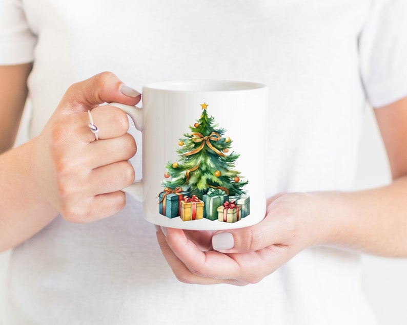 May include: White ceramic mug with a watercolor illustration of a green Christmas tree with gold ornaments and a red bow. The tree is surrounded by wrapped presents with red, green, and gold accents.