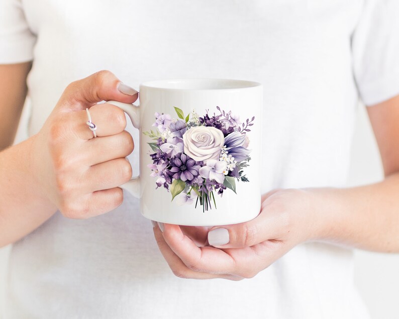 May include: White ceramic mug with a floral design of purple and white flowers. The bouquet includes roses, hydrangeas, and other blooms. The mug is held by a person.