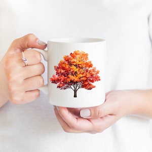 May include: White ceramic mug with a colorful autumn tree design. The tree has orange, red, and yellow leaves.