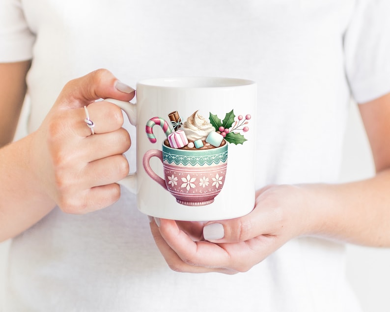May include: White ceramic mug featuring a watercolor illustration of a hot chocolate drink. The mug is decorated with a pink and teal design and filled with whipped cream, marshmallows, and a candy cane. A festive holiday theme.