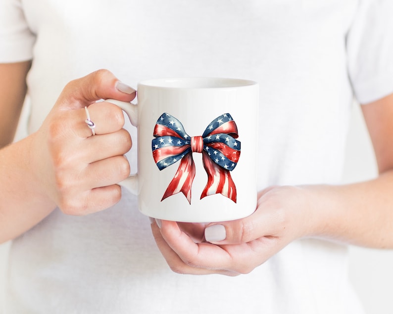 May include: White ceramic mug with a red, white, and blue bow printed on the front. The bow is made of ribbon with stars and stripes.