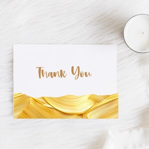 May include: A white card with the words "Thank You" printed in brown text. The card is decorated with a gold abstract design.