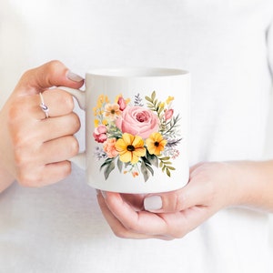 May include: White ceramic mug with a floral design featuring pink, yellow, and orange flowers. The flowers are painted in a watercolor style and are arranged in a bouquet.