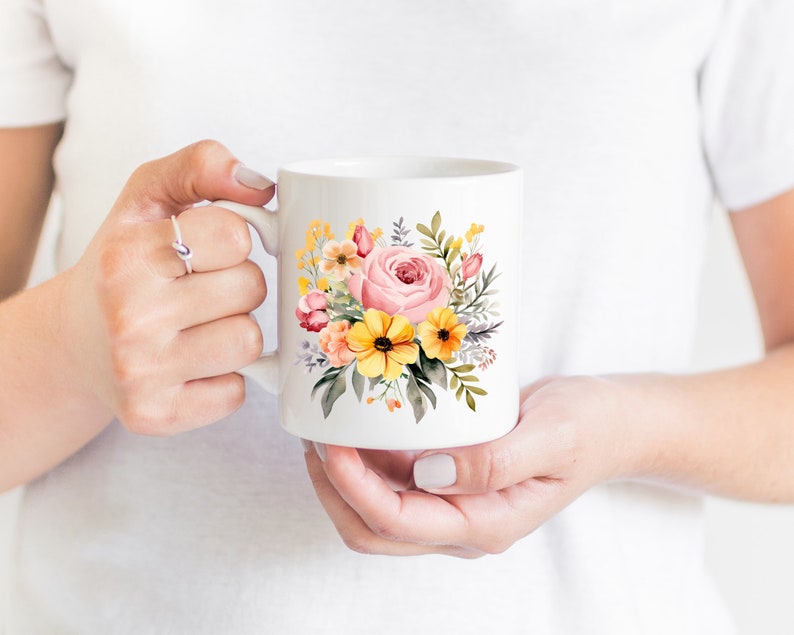 May include: White ceramic mug with a floral design featuring pink, yellow, and orange flowers. The flowers are painted in a watercolor style and are arranged in a bouquet.
