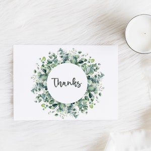 May include: A white card with a green eucalyptus wreath around a circle that says "Thanks" in black script.